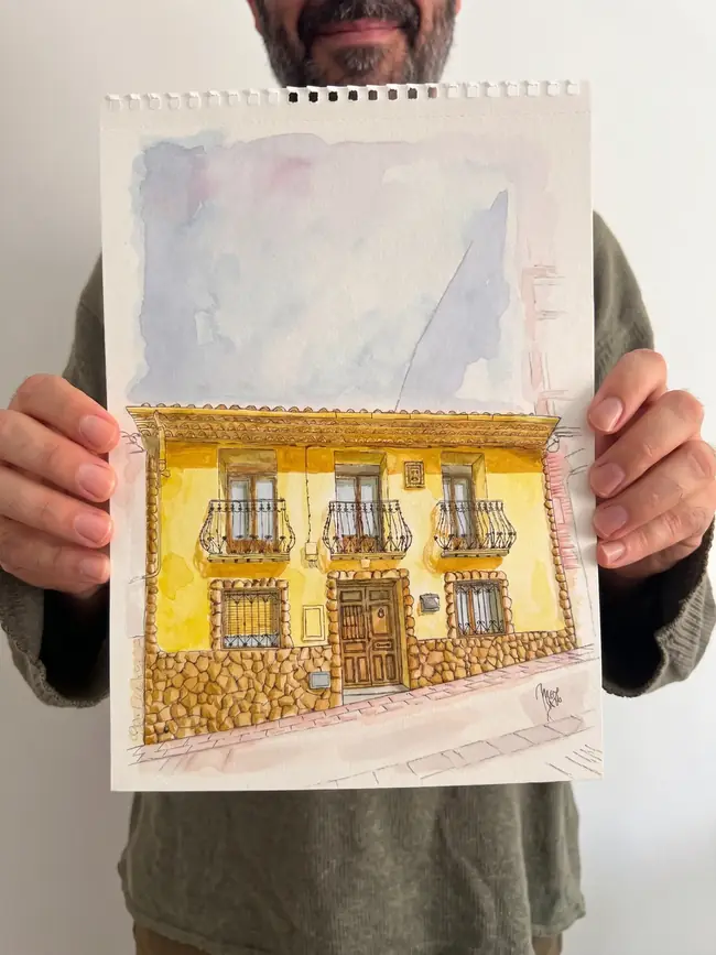 Pedro sujetando una acuarela original de una fachada de casa de pueblo pintada a mano